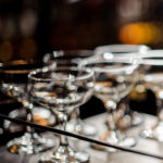 Orange peel being expressed over a cocktail. Rental glassware occupies the background.